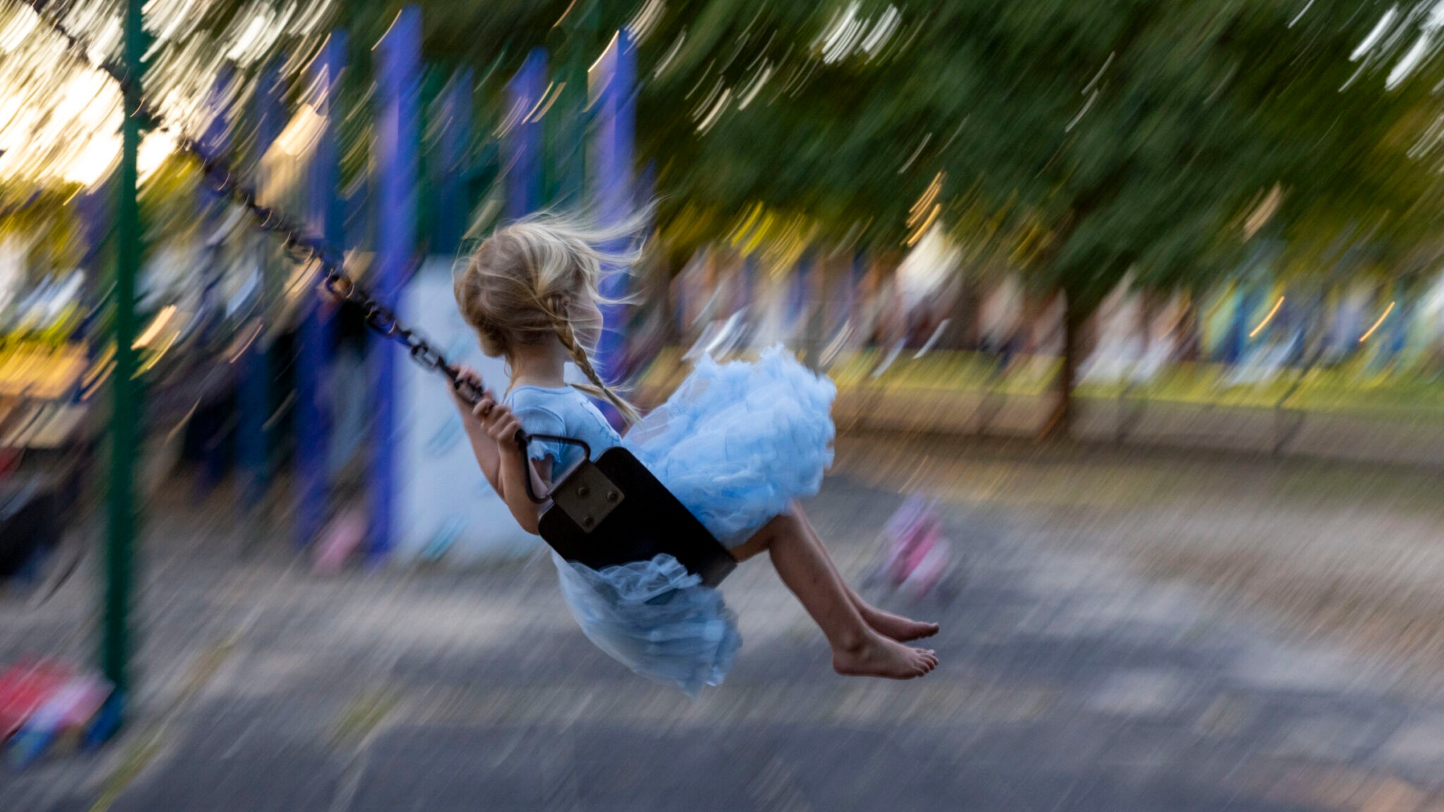 A little blonde girl is on a swing in a playground