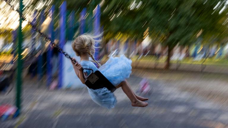 A little blonde girl is on a swing in a playground