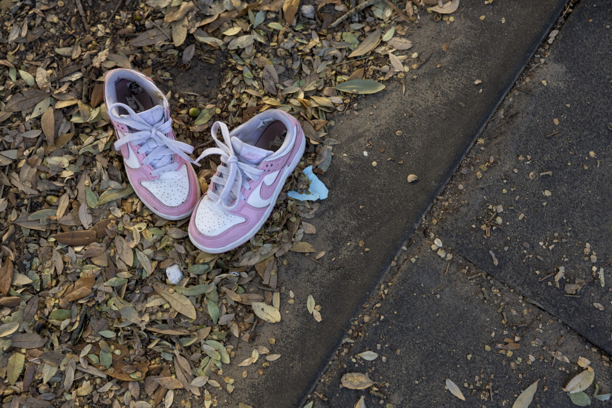 Two pink child size sneakers are seen on a sidewalk