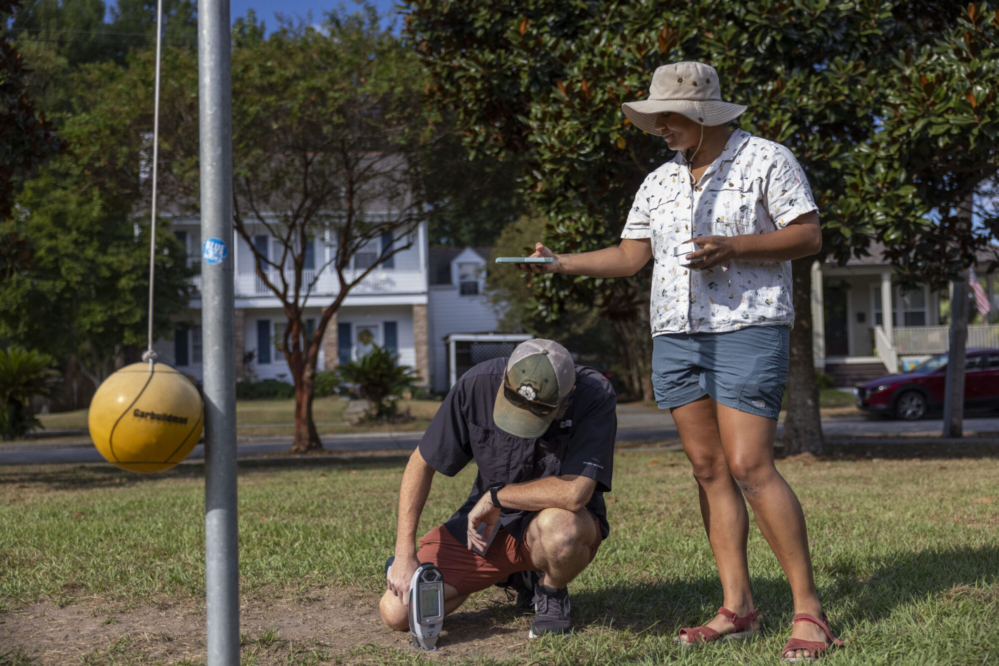 A woman and man stand in a park holding instruments to measure lead