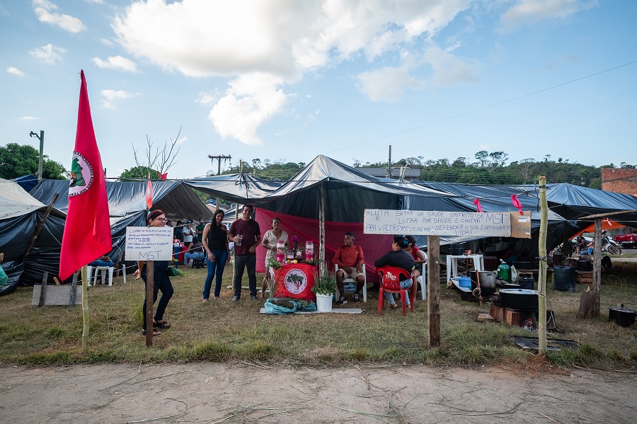 People hold signs in front of a camp with tents