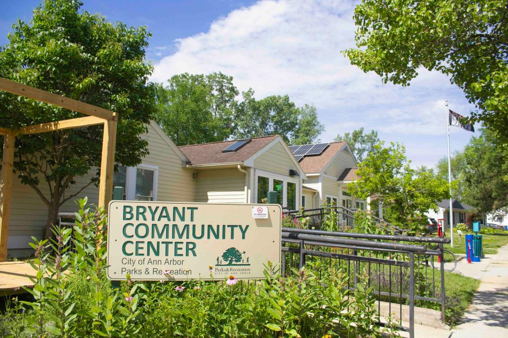 A building with solar panels stands on a lushly tree-lined street, with a sign reading Bryant Community Center