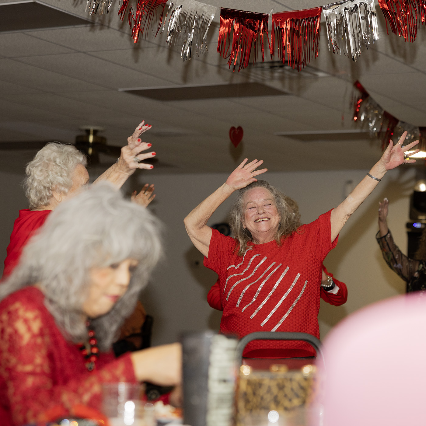 A group of elderly women in red smile and wave their hands in the air on the dance floor