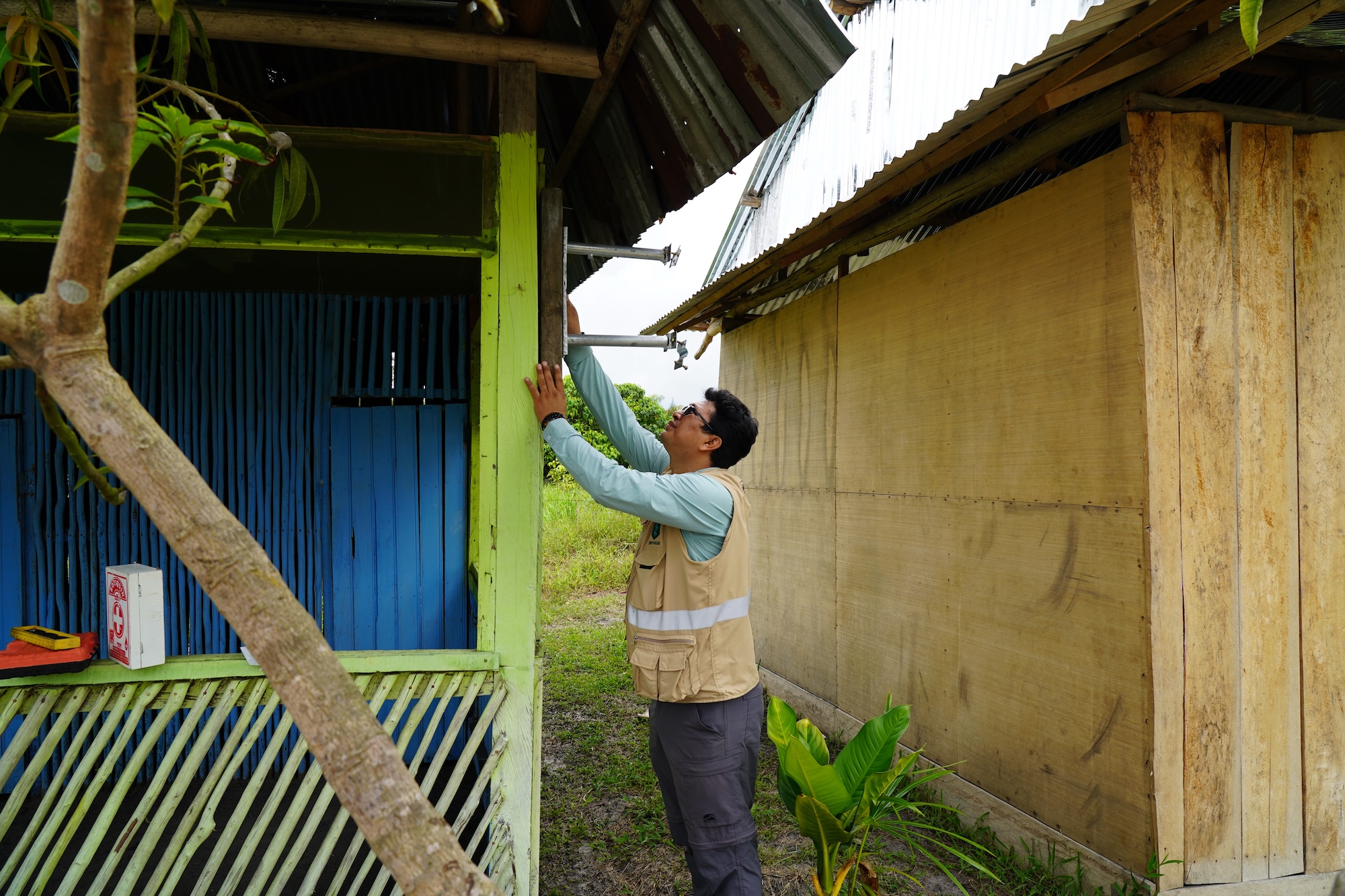 A man in a vest checks a monitor on the wall of a house