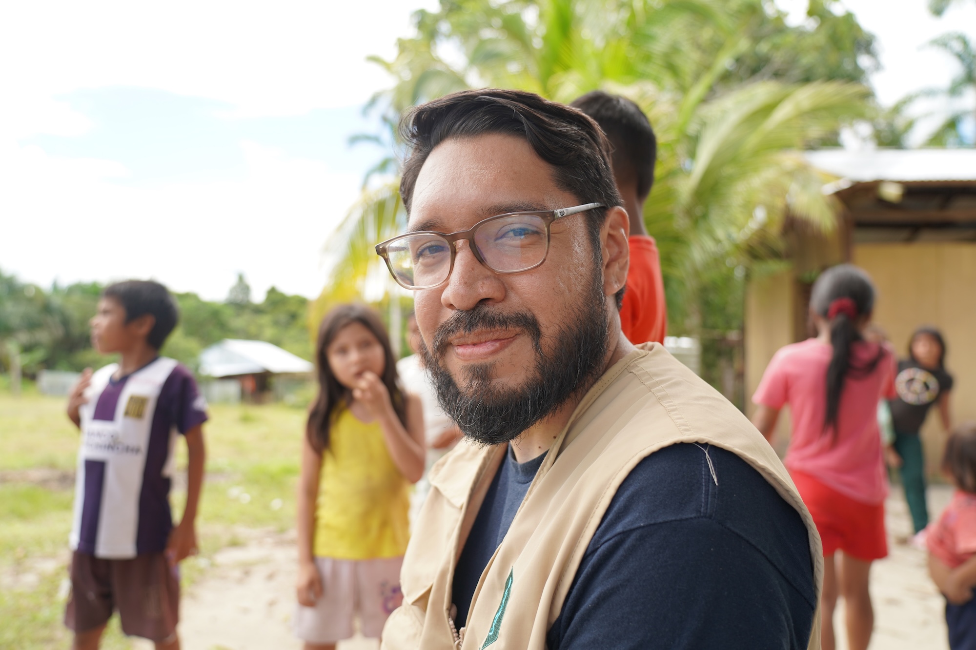 A man with glasses and a beard looks into the camera while children hover nearby