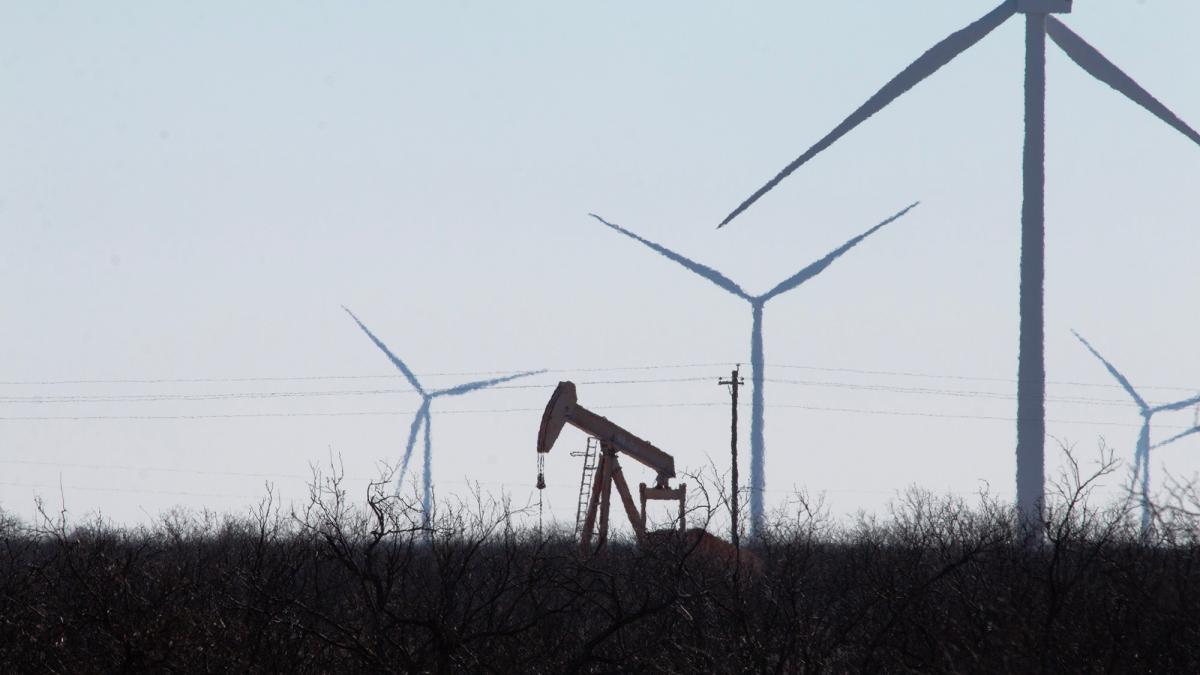 An oil pumpjack is seen in the same field as several wind turbines