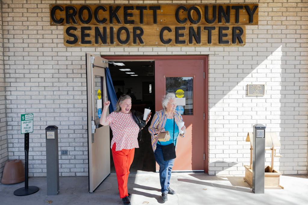 Two older women walk gleefully out of a building labeled Crockett County Senior Center