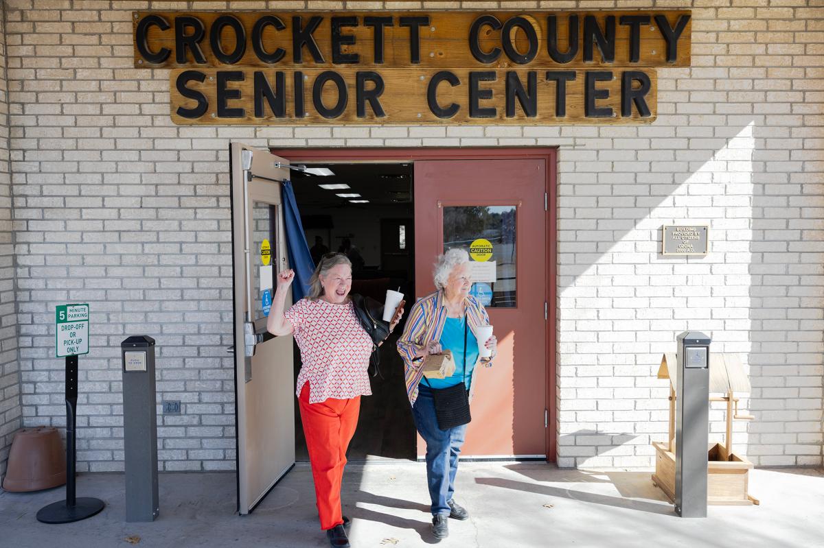 Two older women walk gleefully out of a building labeled Crockett County Senior Center