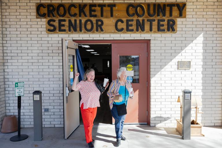 Two older women walk gleefully out of a building labeled Crockett County Senior Center