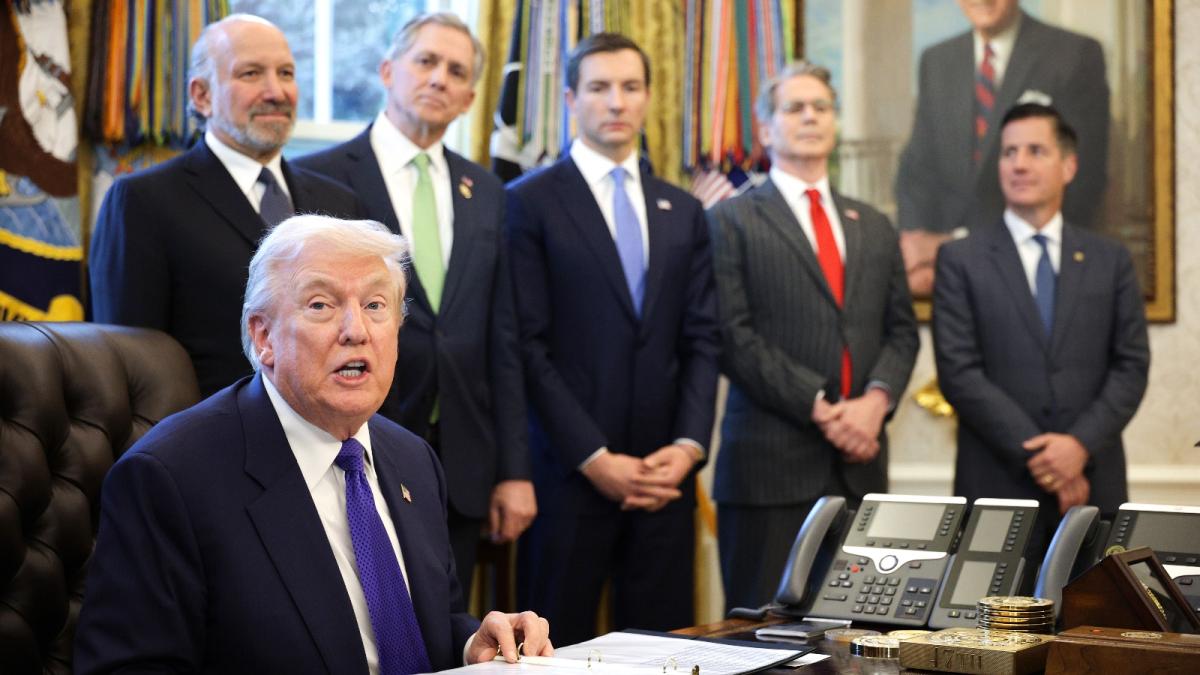Trump looks toward the camera in the Oval Office, behind him stand five men.