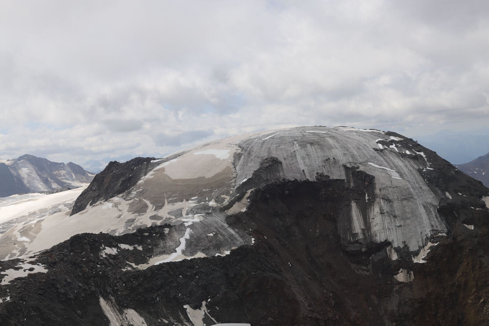 A soot-colored mountainside where an icy glacier is receding