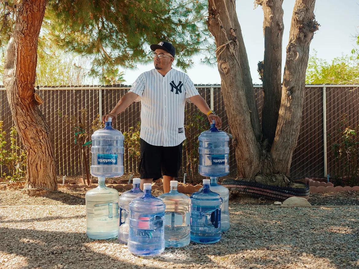 A man wearing a Yankees jersey holds up huge water bottles