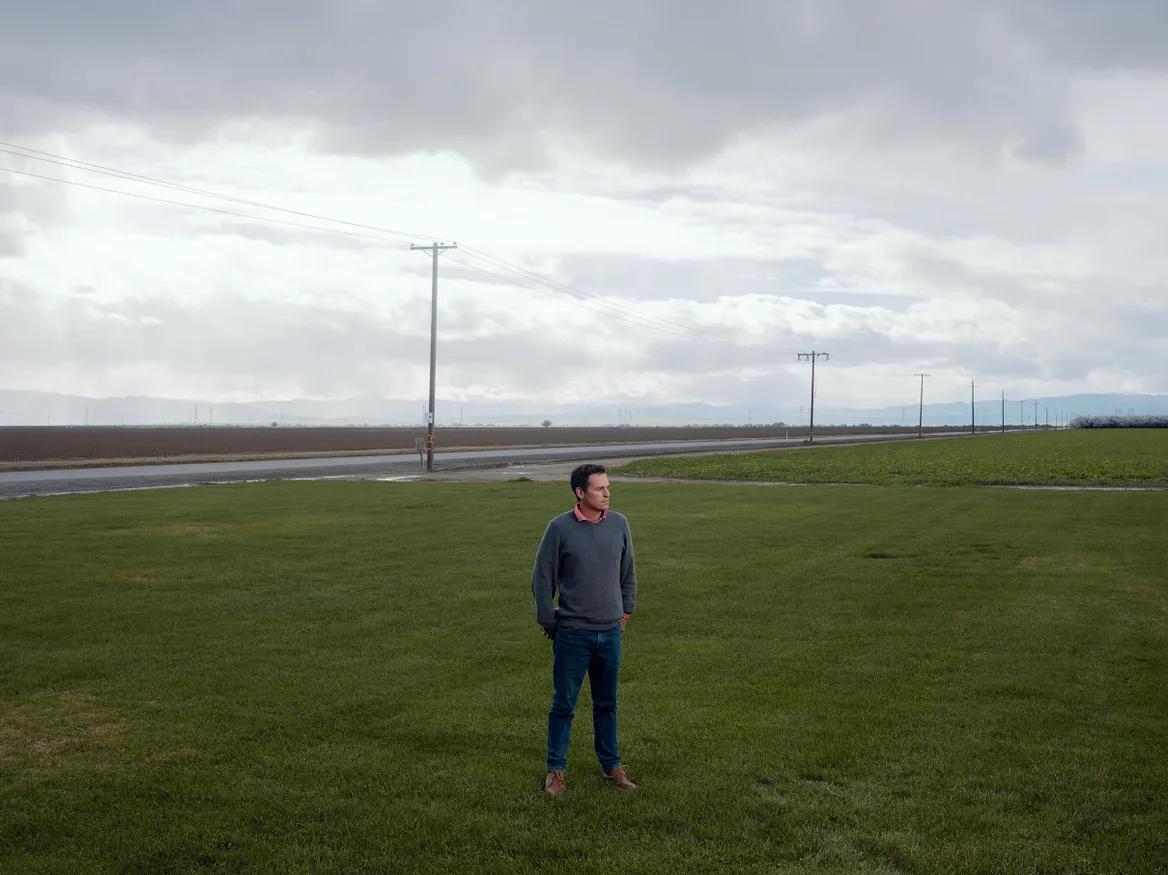 A man stands in a green field under cloudy skeis