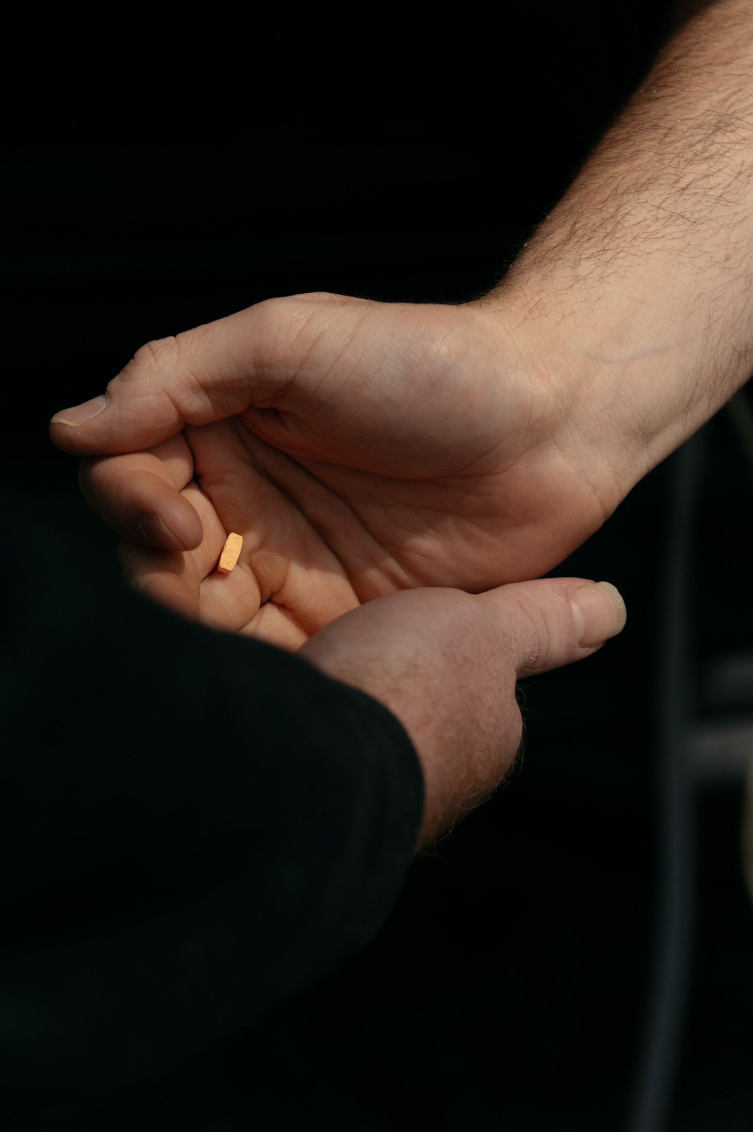 A closeup photo of a person's hand giving an orange tab of Suboxone to another person.