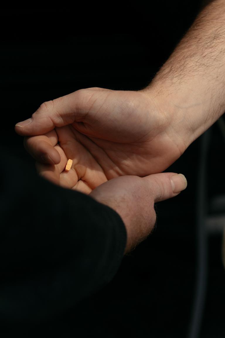 A closeup photo of a person's hand giving an orange tab of Suboxone to another person.