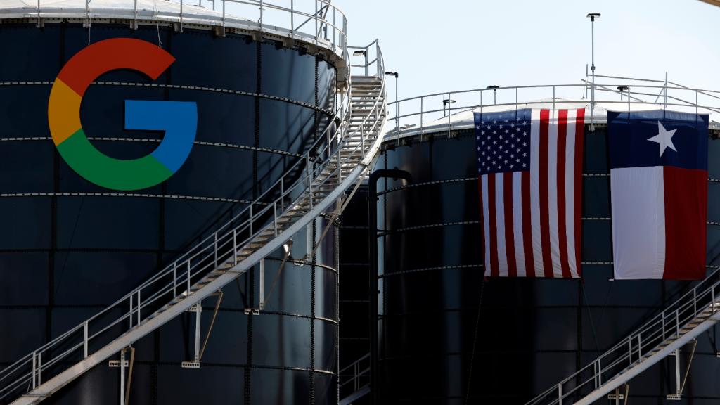 Two cooling towers have a Google logo on them and a Texas and US flag draped over another