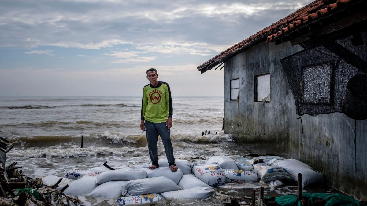 A man stands on sandbags next to a building as waves lap behind him