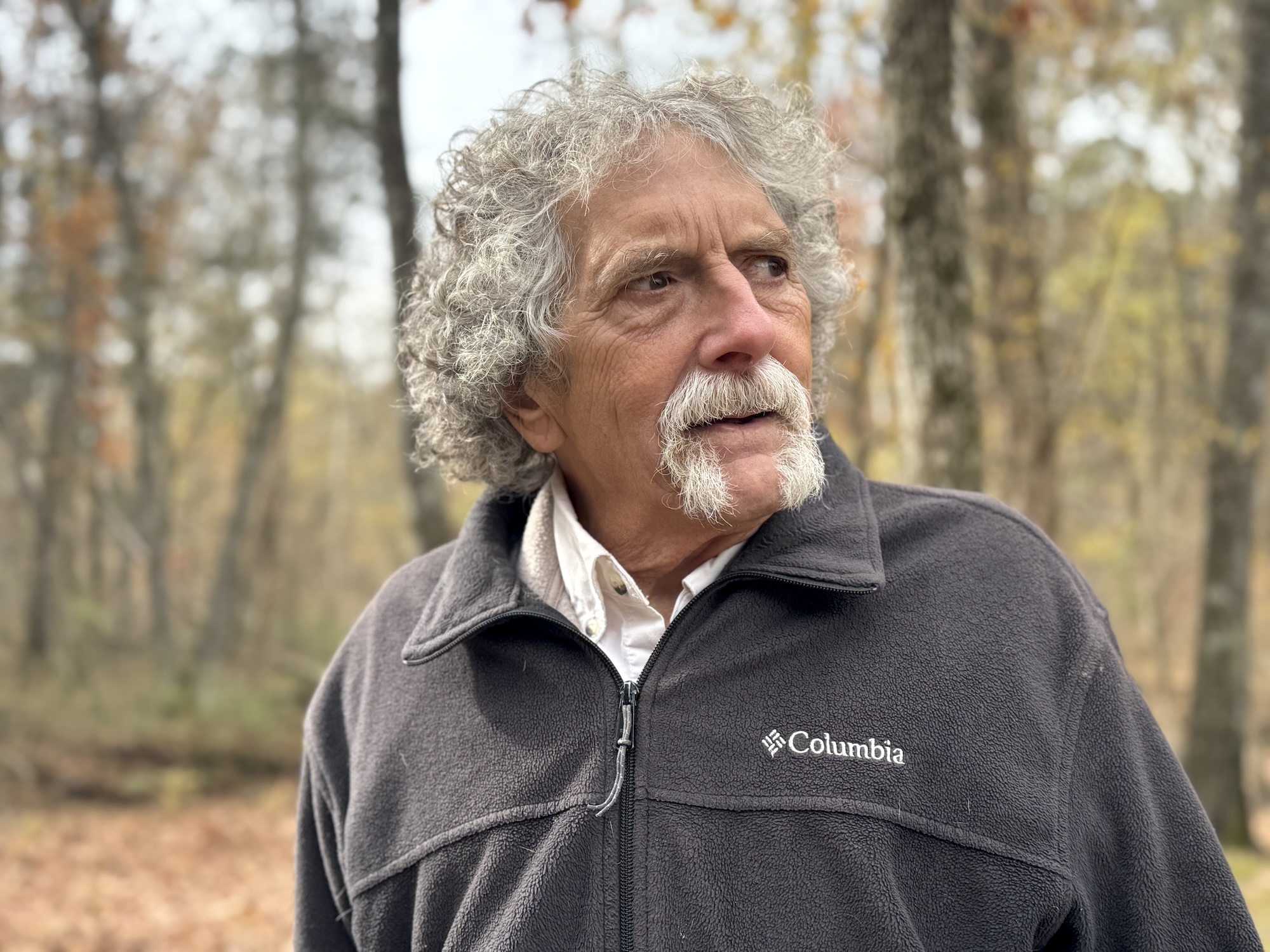 A man with white hair and a beard looks out at a beautiful forest