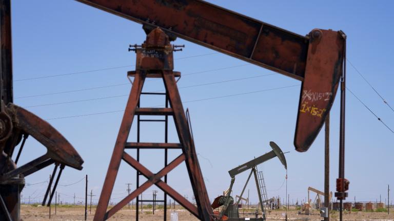 Reddish pumpjacks stand in the desert