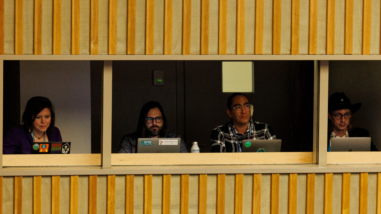Reporters sit behind laptops in a booth