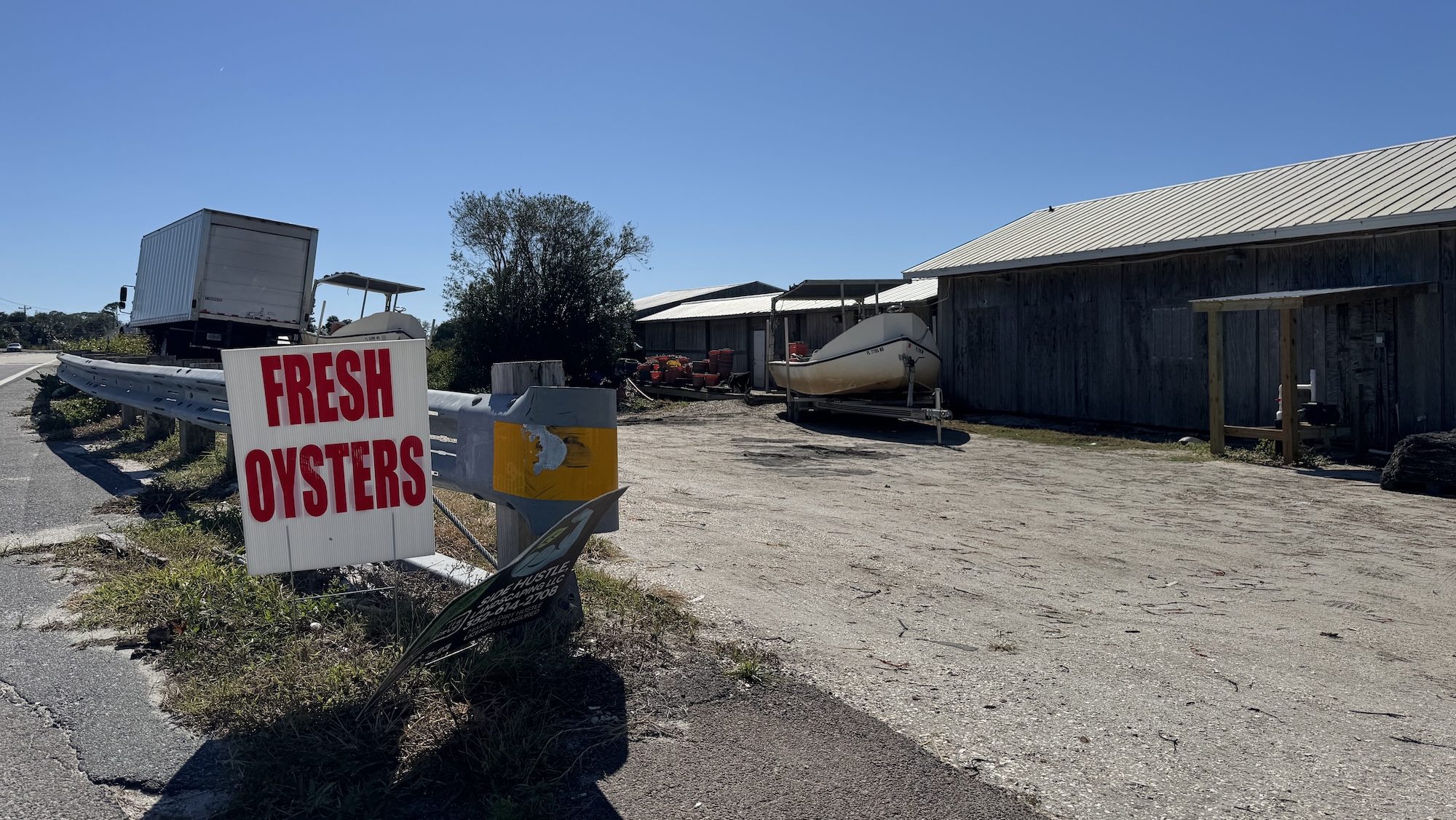 A sign says fresh oysters near a shack on the beach