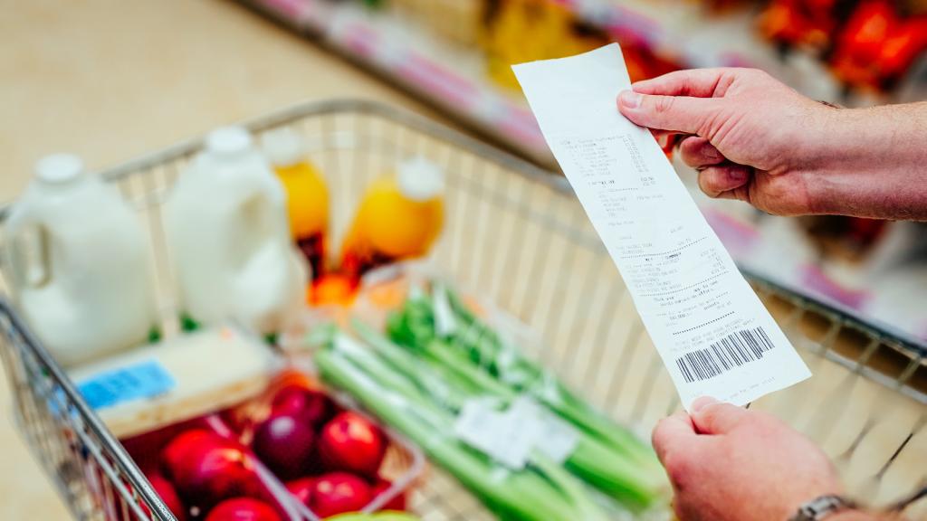 Photo of someone holding a grocery receipt over a cart full of food