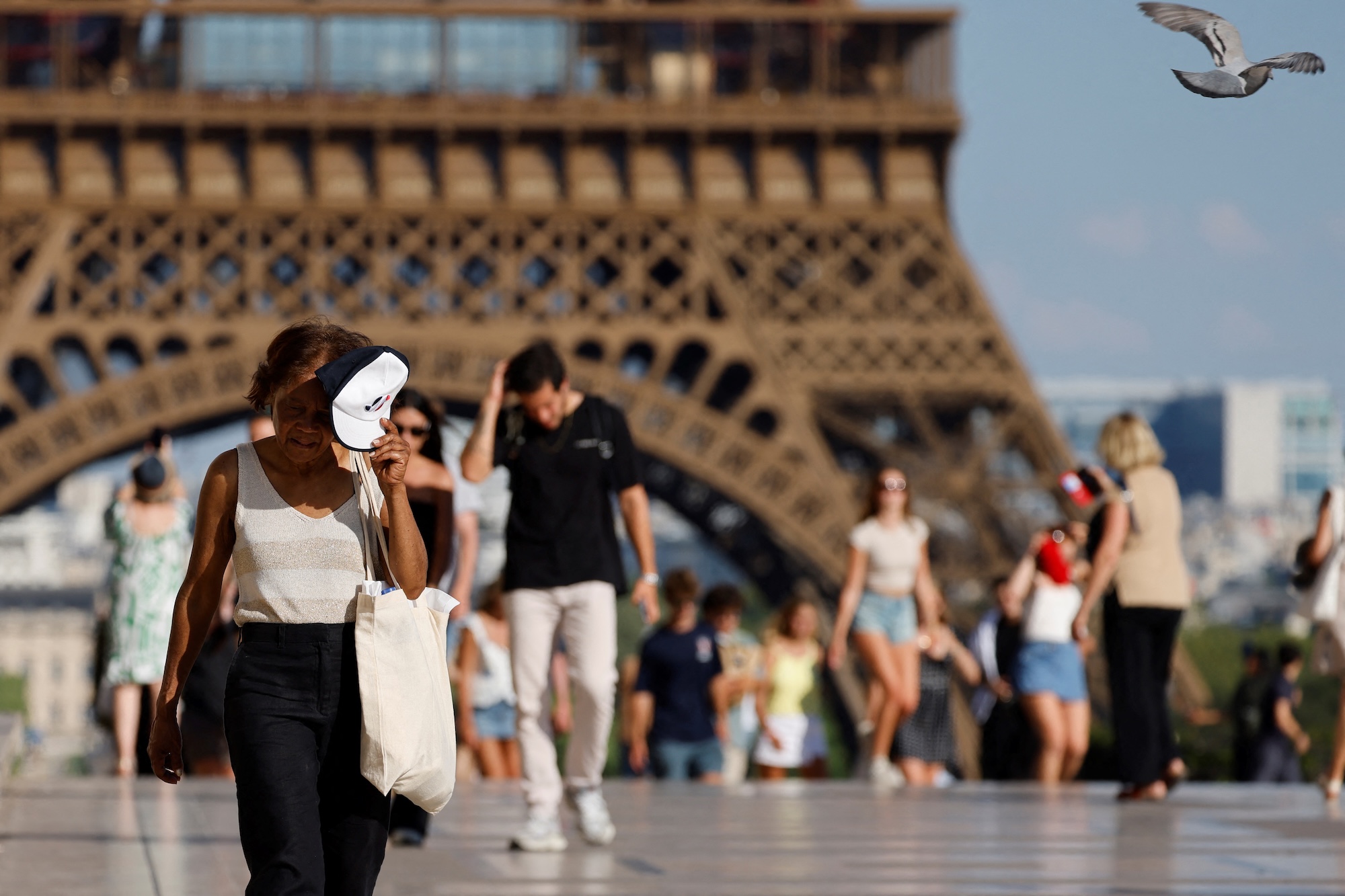people shield their faces from the sun as they walk near the Eiffel tower in Paris