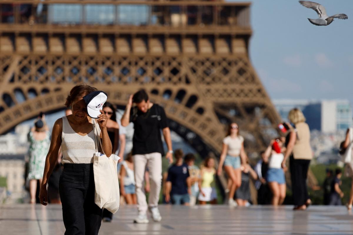 people shield their faces from the sun as they walk near the Eiffel tower in Paris