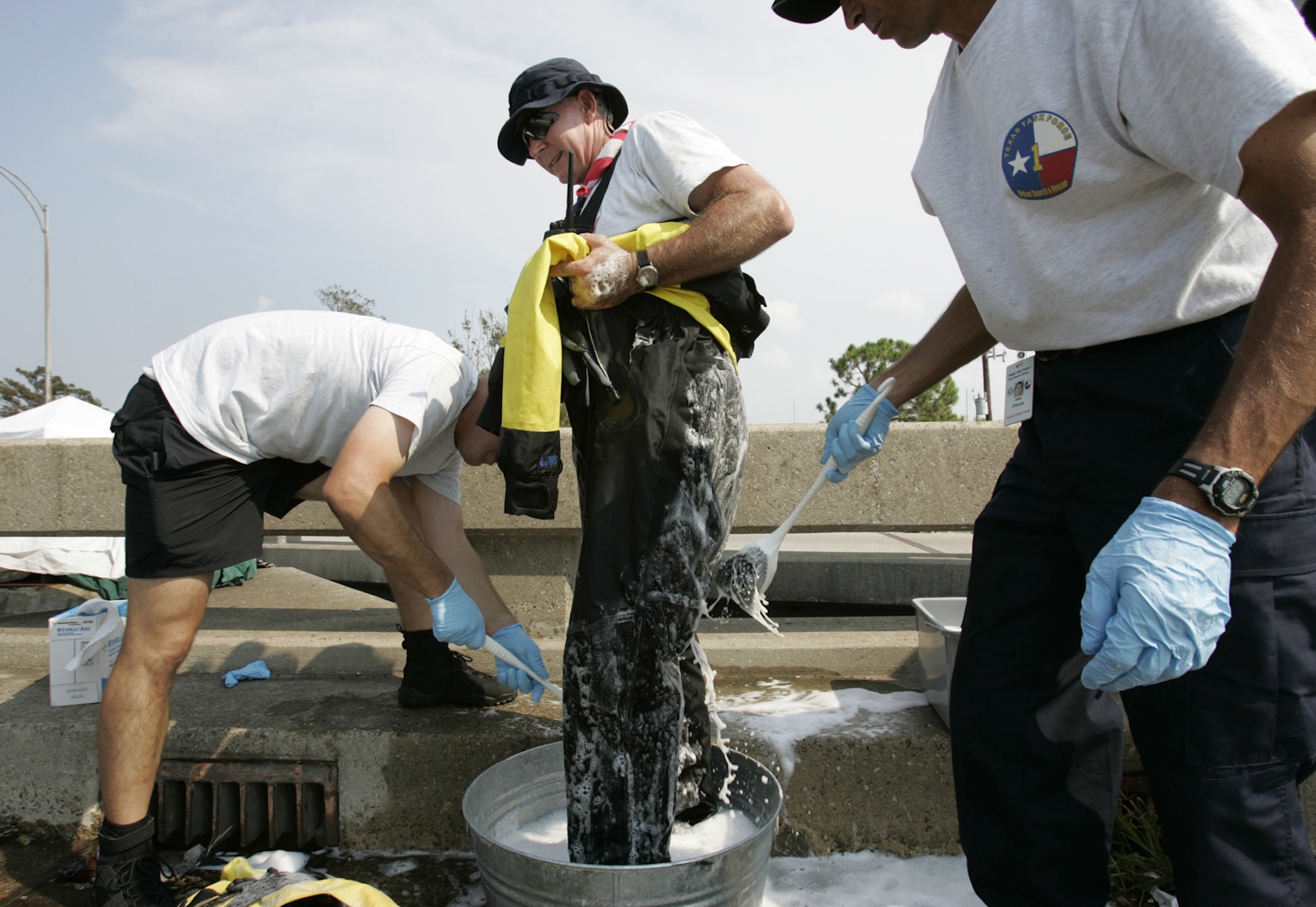 a man is washed down with disinfectant by people in official t-shirts with logos resembling the texas state flag
