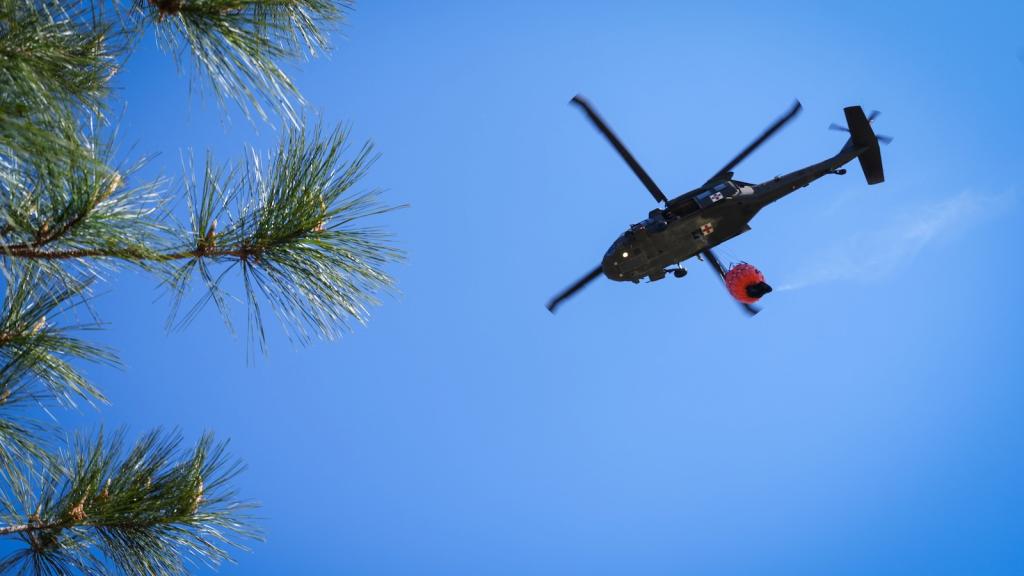 A helicopter pulls water from Kade Lake to respond to a growing wildfire near Cleveland, Texas, on March 20, 2025.