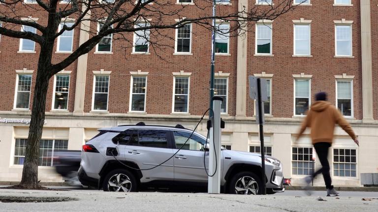A pedestrian walks past a Toyota RAV4 EV plugged in outside city hall in Portland, Oregon.