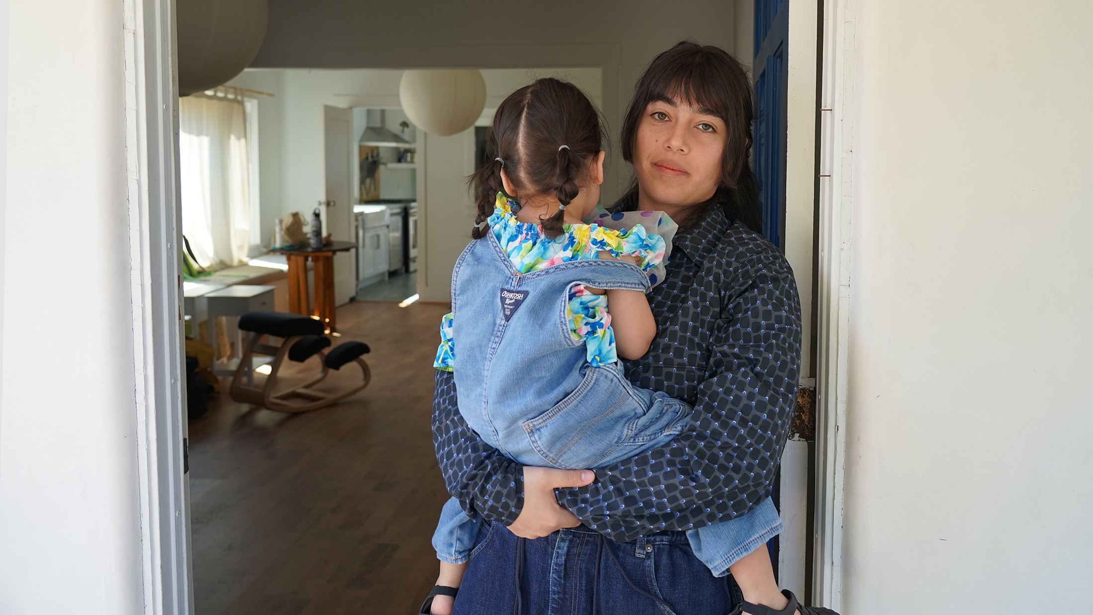 A woman holds a young child in a doorway.