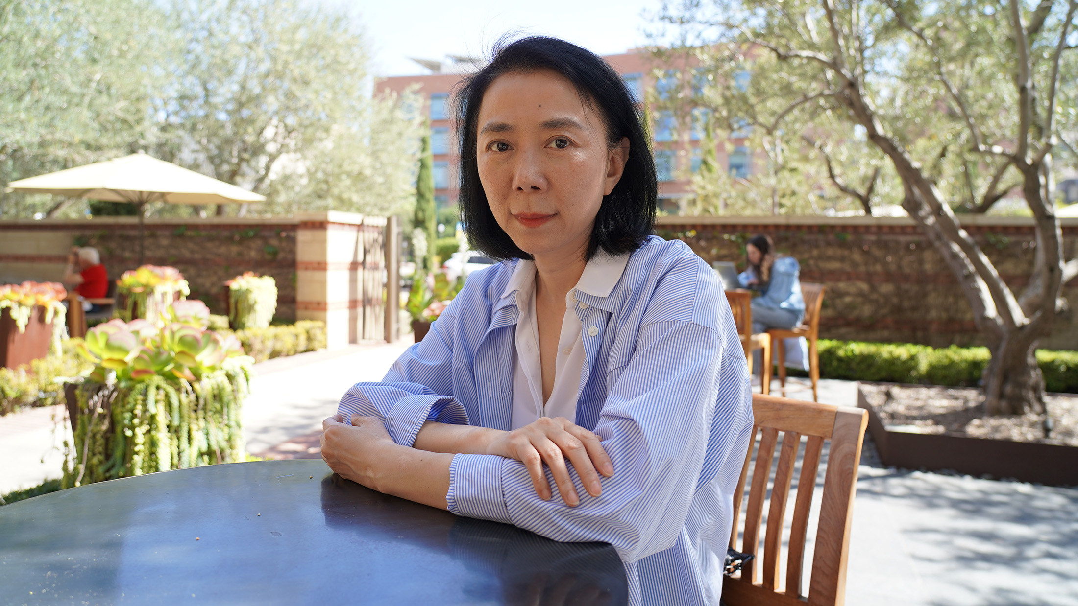 A woman waring a light blue shirt sits at an outdoor cafe table.
