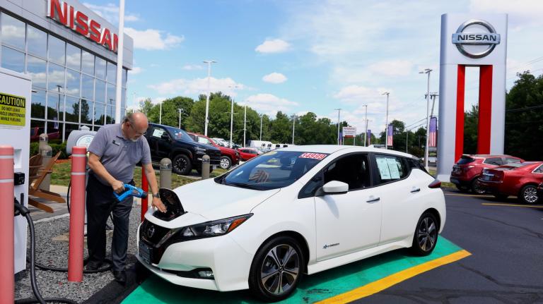A salesman at a Nissan dealership plugs in a used Nissan Leaf electric vehicle.