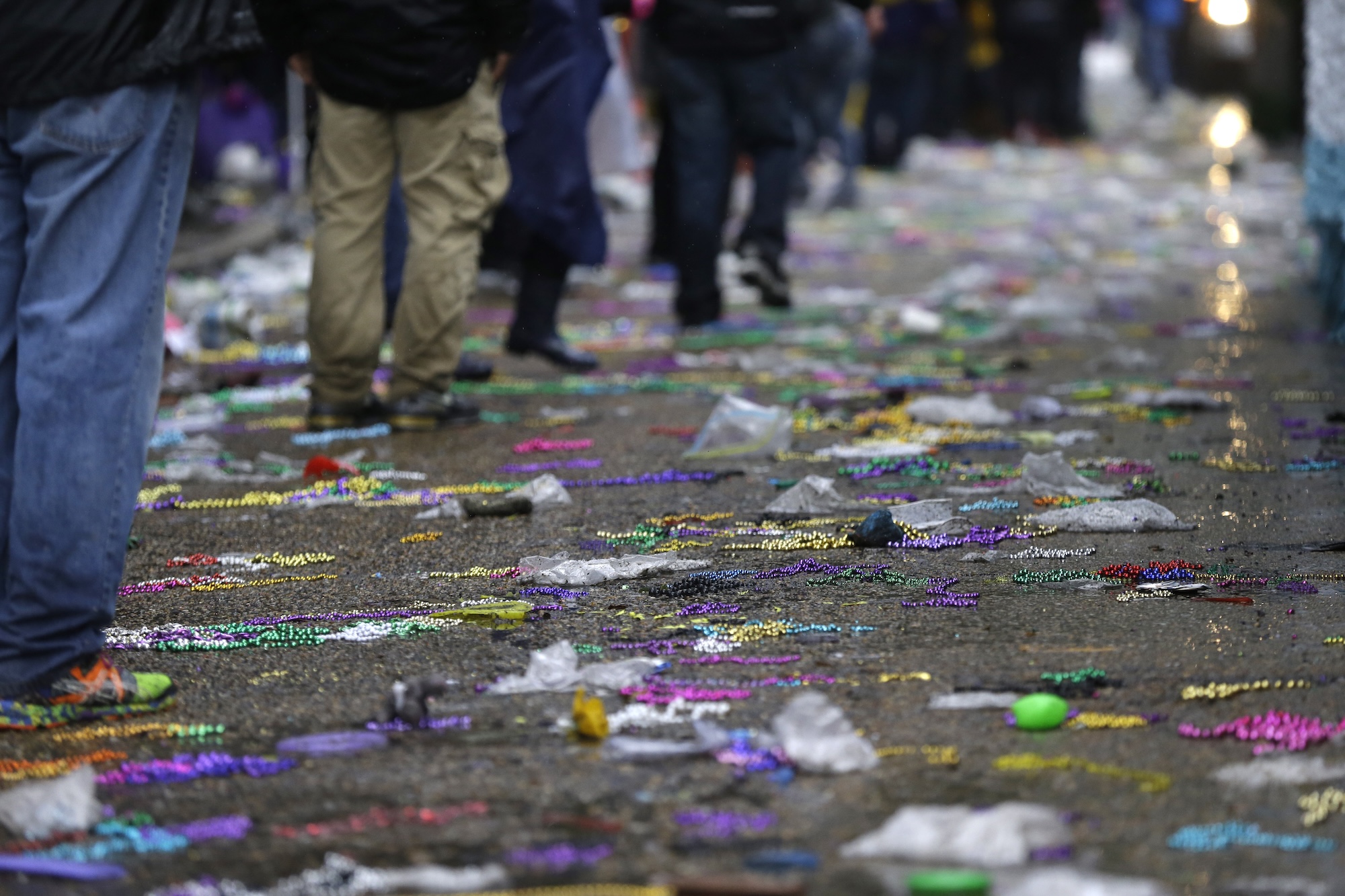 people walk alongside a street covered in colorful plastic beads and trash