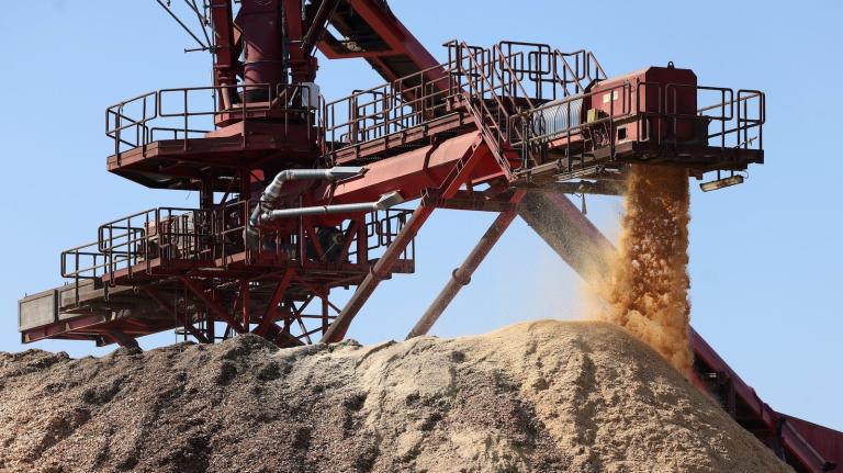 A towering pile of sawdust beneath machinery at a wood pellet mill.