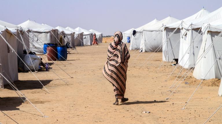 A woman walks alone among white tents in a desert