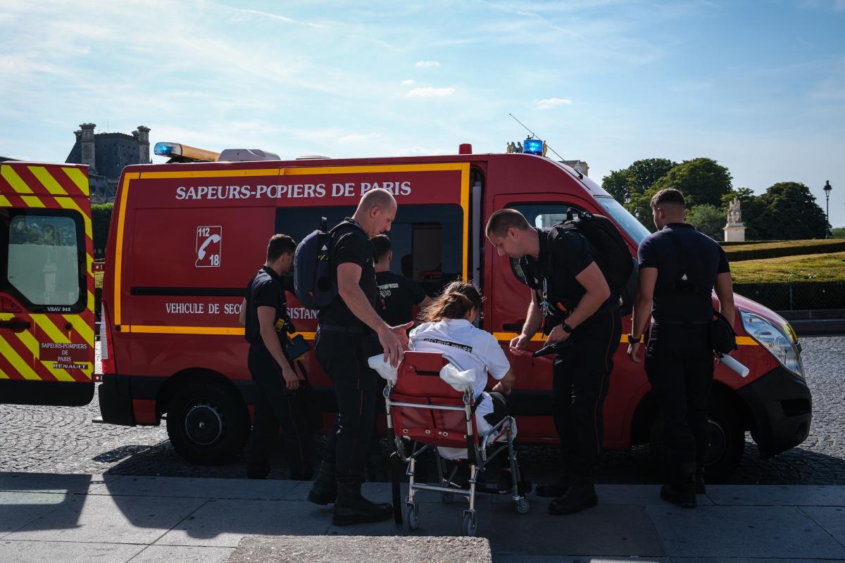 people in blue uniforms load a person on a stretcher into an ambulance with french writing on the side