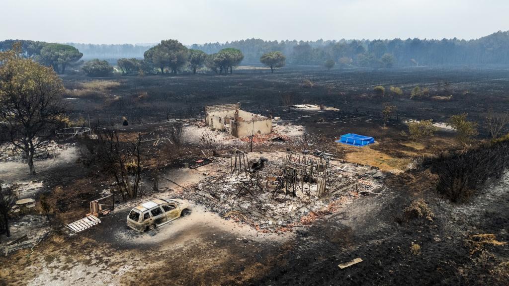 a blackened landscape of farmland with the shape of a house and car reduced to rubble in the foreground.