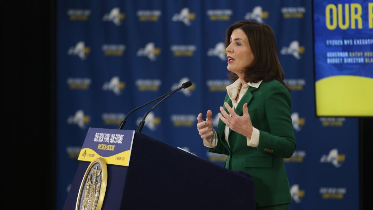 A woman in a green suit jacket speaks at a podium