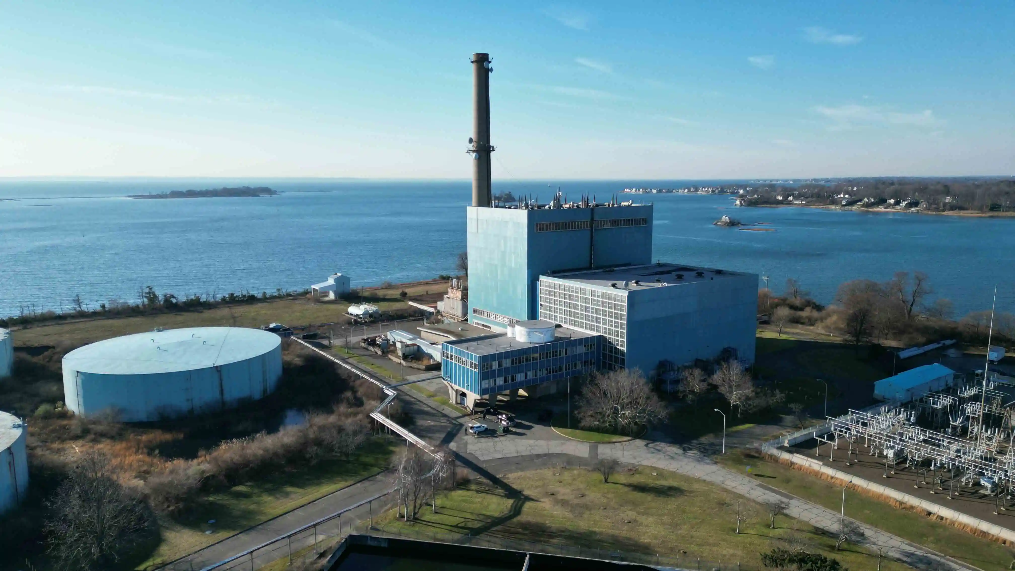 An aerial view of a power plant with a tall smokestack standing over the water