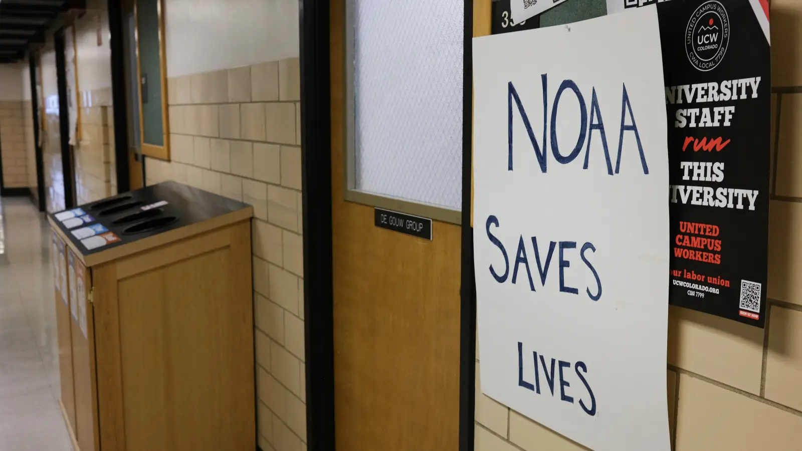 Photo of a sign reads "NOAA Saves Lives" next to a door in a hallway