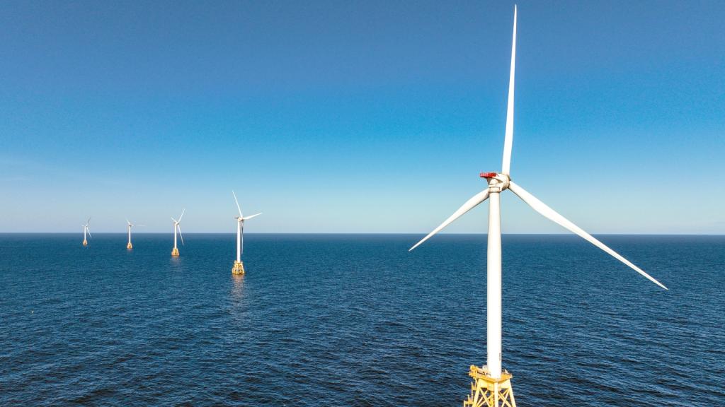 White wind turbines stand in the middle of the ocean