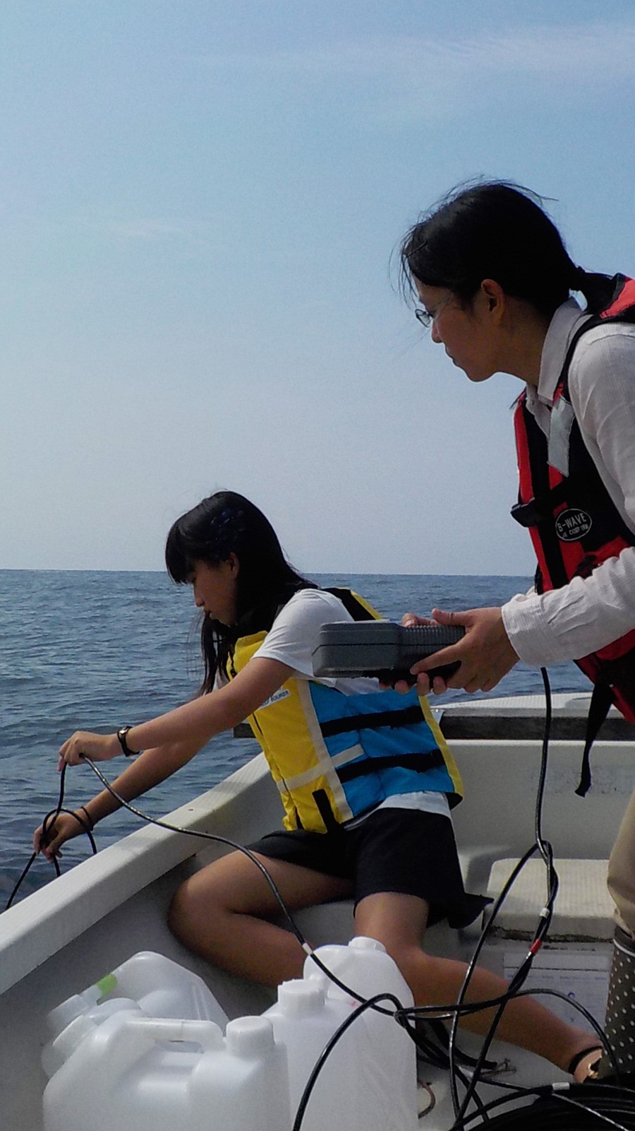 An adult woman and a child collect seawater off the side of a boat
