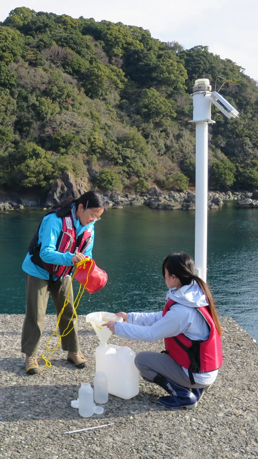 An adult woman and a child collect seawater on a dock