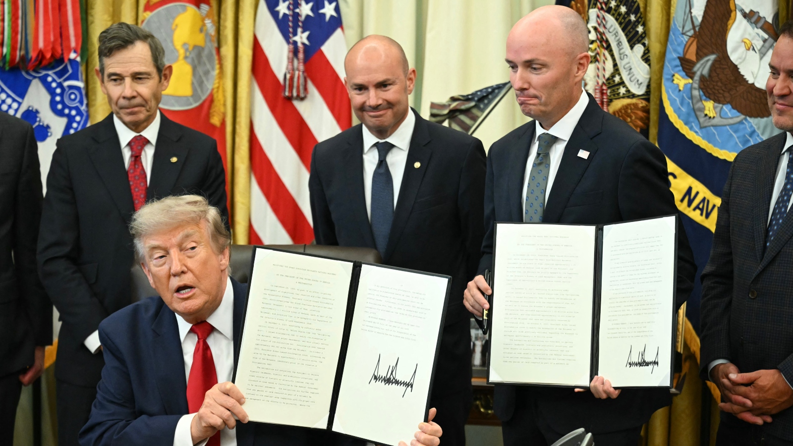 Men sit at a table holding open folders