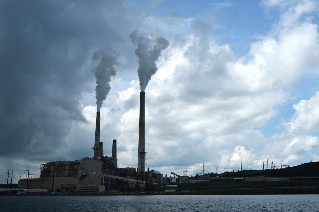 Smoke billows out of the stacks at a coal plant against a cloudy blue sky