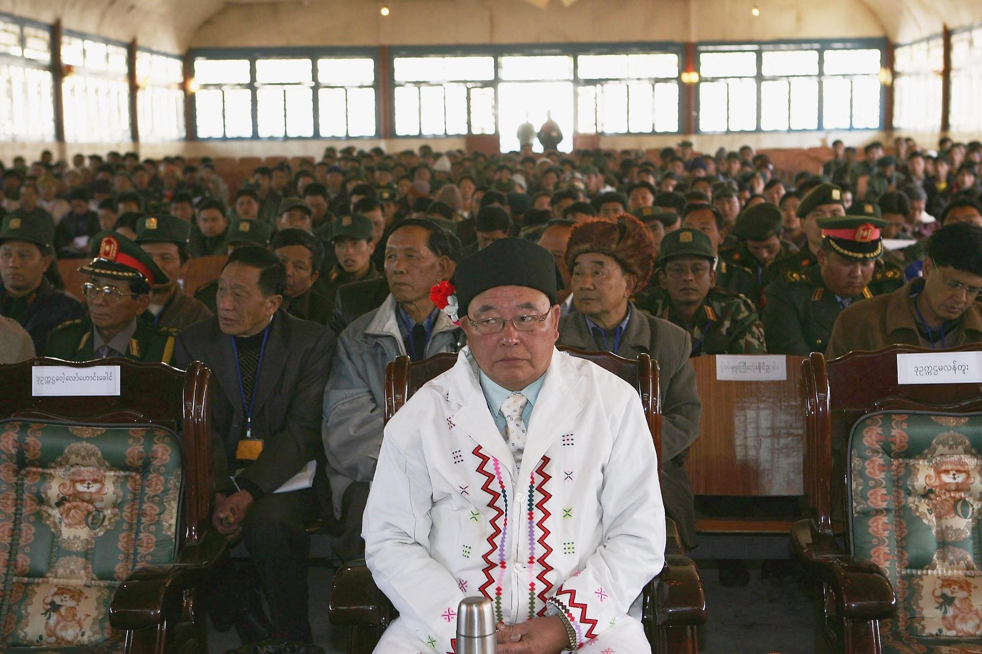 A main in ceremonial white garb sits in front of a crowd