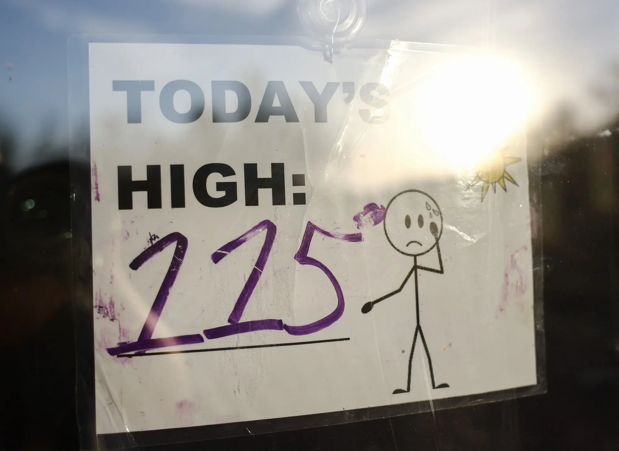 A sign posted in a window reads Today's High 115 with a frowning stick figure
