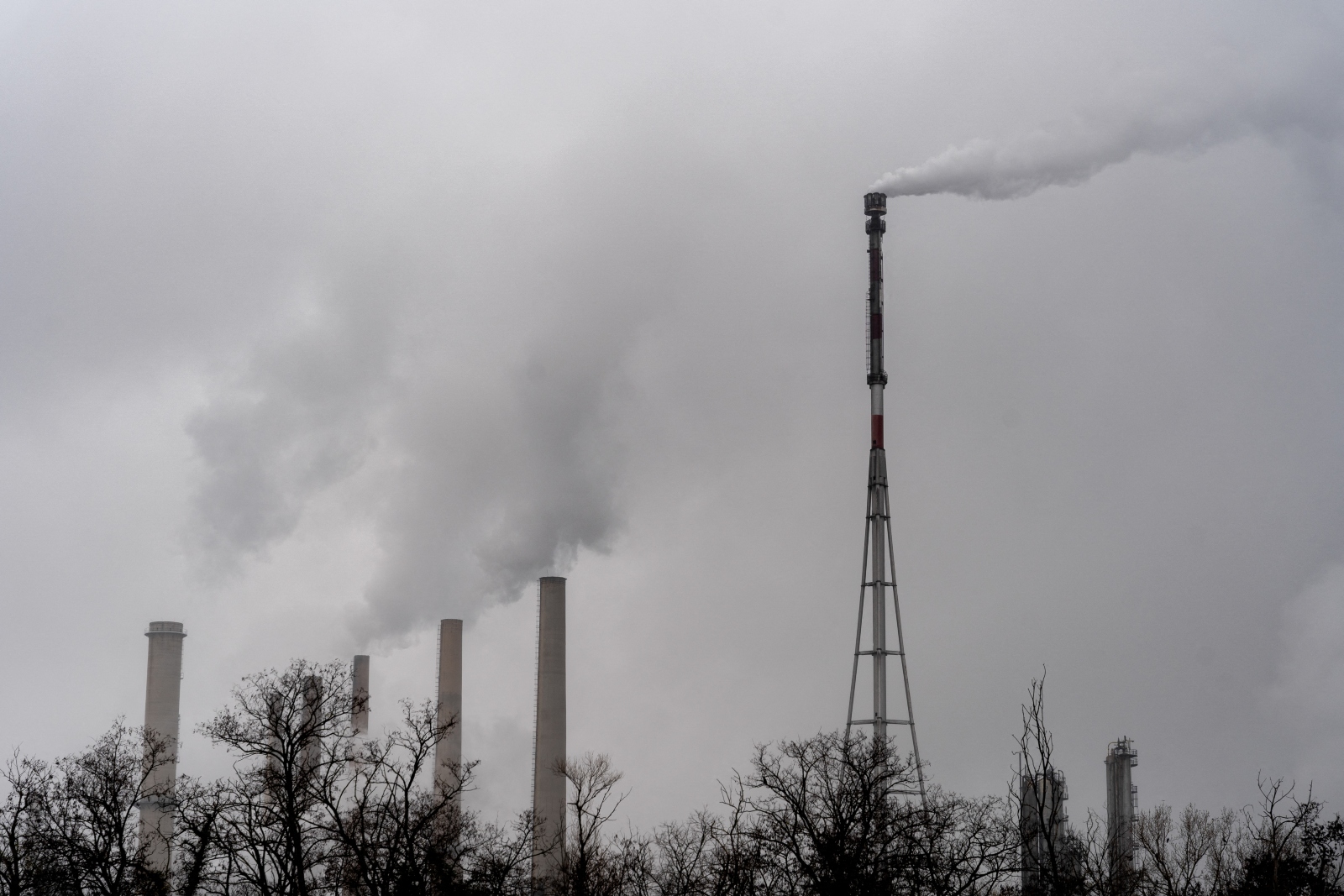 Black-and-white photo of the chimneys at a refinery emitting thick white smoke under a cloudy sky